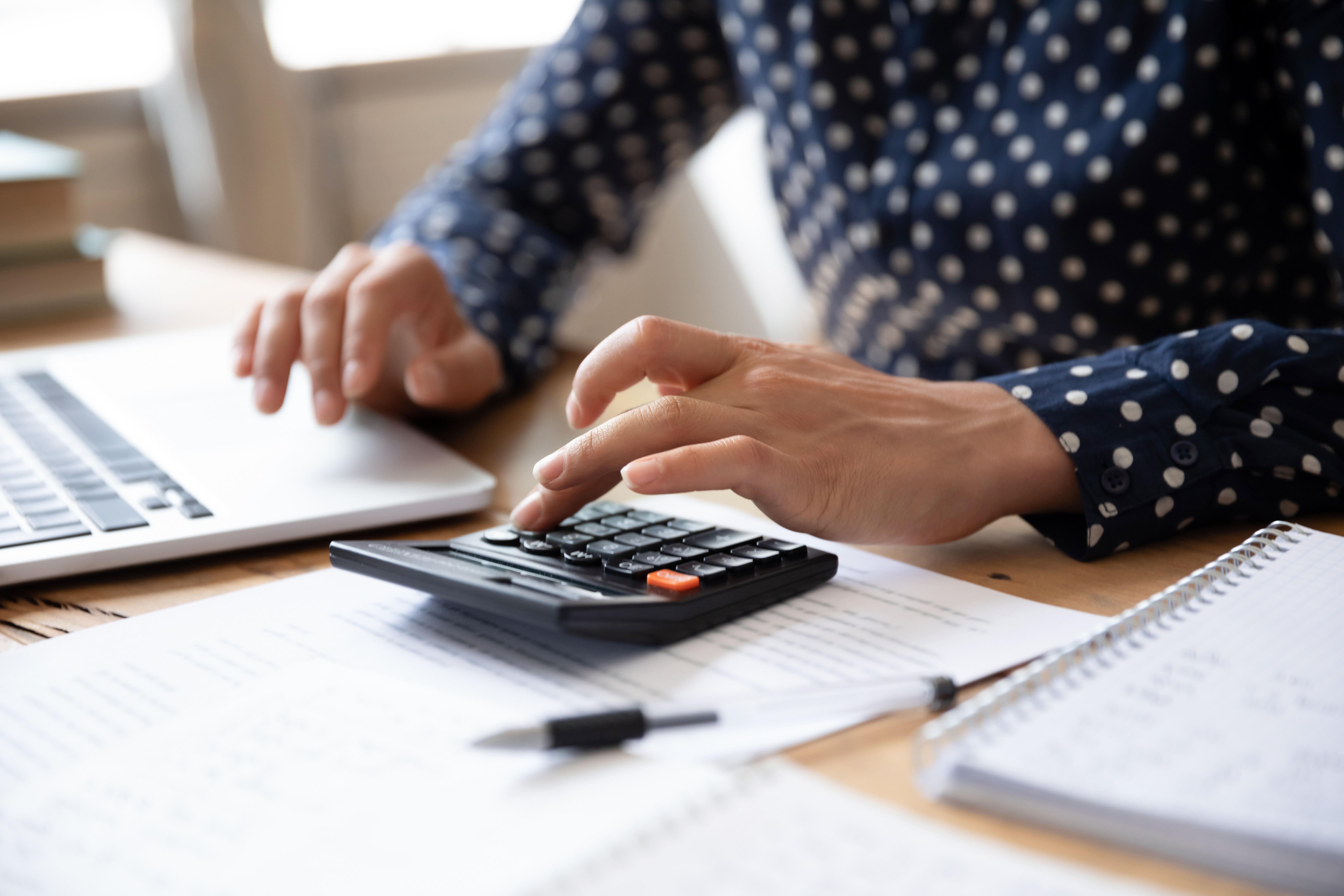 Close up Indian woman planning budget, using calculator and laptop Iemand zet een handtekening